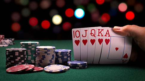 person holding cards with poker chips on table, faded black with lights in background